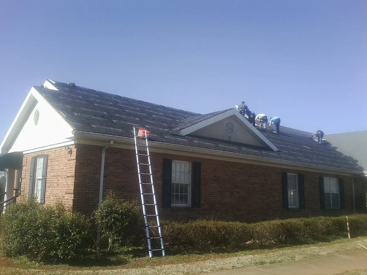 Crew tearing shingles off a brick ranch roof with a ladder set — Emergency Roof Repair work by our crew in Ocean View