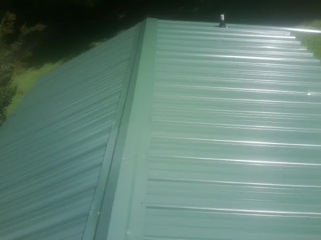 New green metal panels meeting at the ridge of a roof — Flat Roof Repair work by our crew in Ocean View