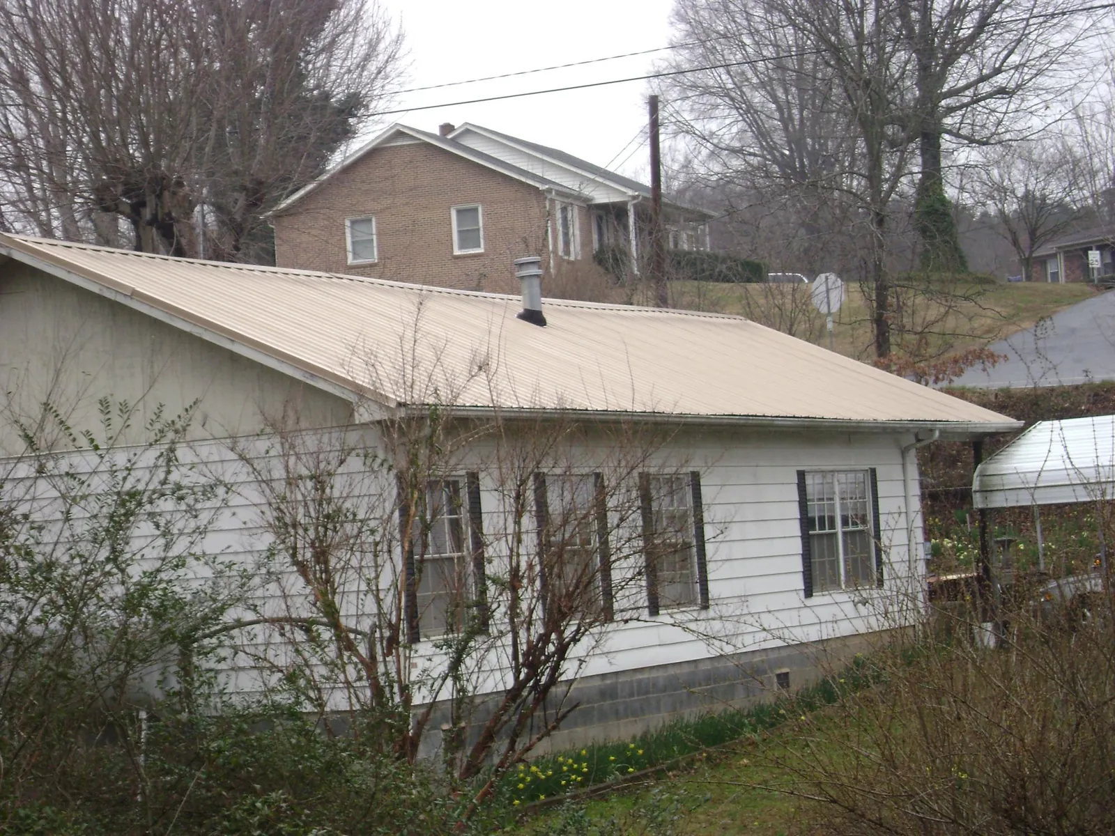 Tan metal roof on a white sided house set into a hillside — Commercial Roofing by Roofing Brothers in Ocean View